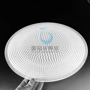 White gloved hand holding a round, translucent Fused Quartz sieve plate with a dense array of small, precisely drilled holes